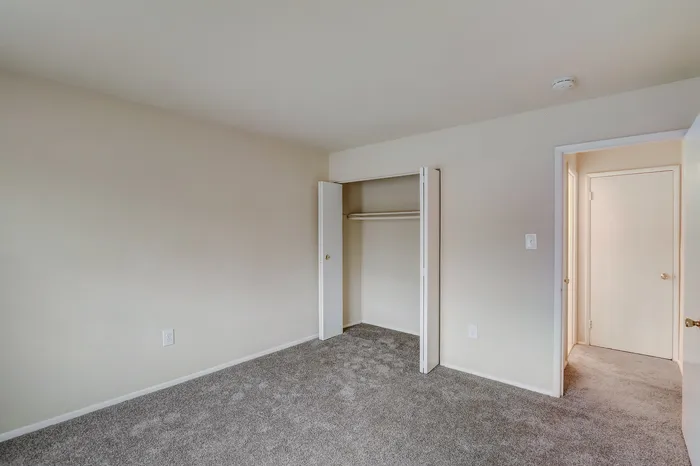 Bright bedroom with fresh carpet, neutral walls, and a spacious closet, offering a cozy and inviting atmosphere.