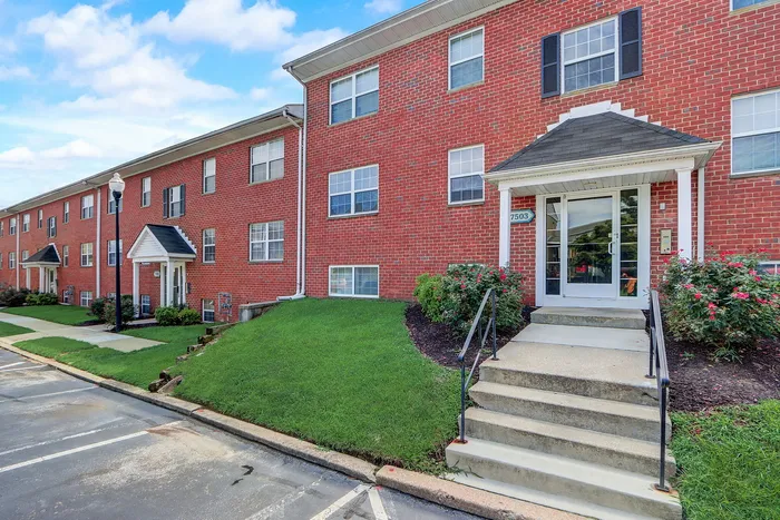 Charming red brick apartment building with a well-maintained lawn and inviting entrance in a peaceful neighborhood.