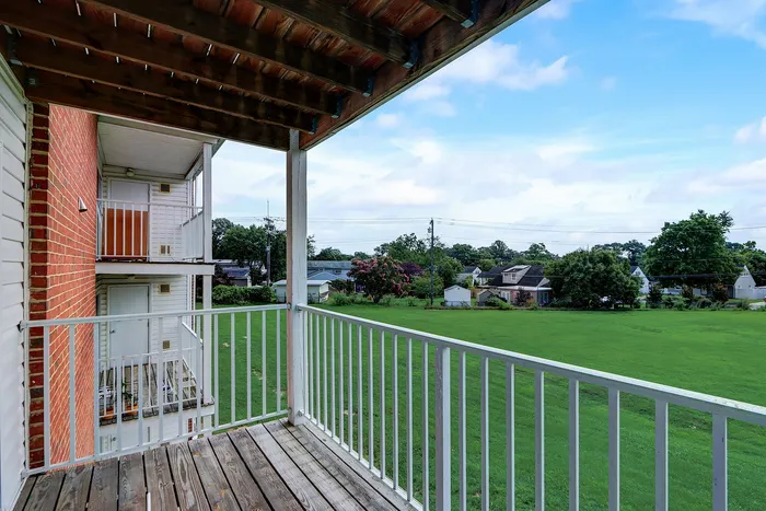 Charming apartment balcony with a scenic view of a lush green field and quaint neighborhood.