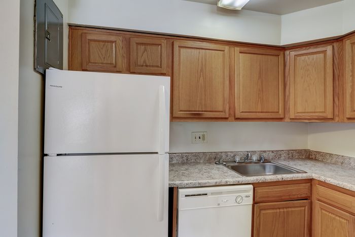 Charming kitchen with warm wooden cabinets, sleek white appliances, and a neat countertop, offering a cozy cooking space.