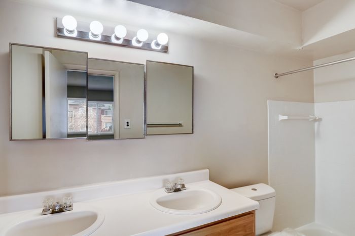 Bright and modern bathroom with dual sinks, large mirror, and shower featuring a sleek white design.