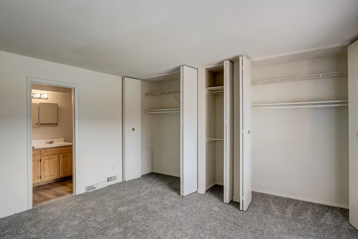 Spacious bedroom with cozy carpet, dual closets, and a glimpse of the elegant ensuite bathroom.
