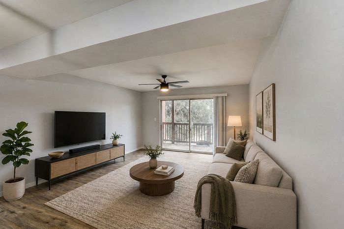 Bright and inviting living room with a modern design, featuring a comfortable beige sofa, sleek TV unit, and large sliding glass doors leading to a balcony.