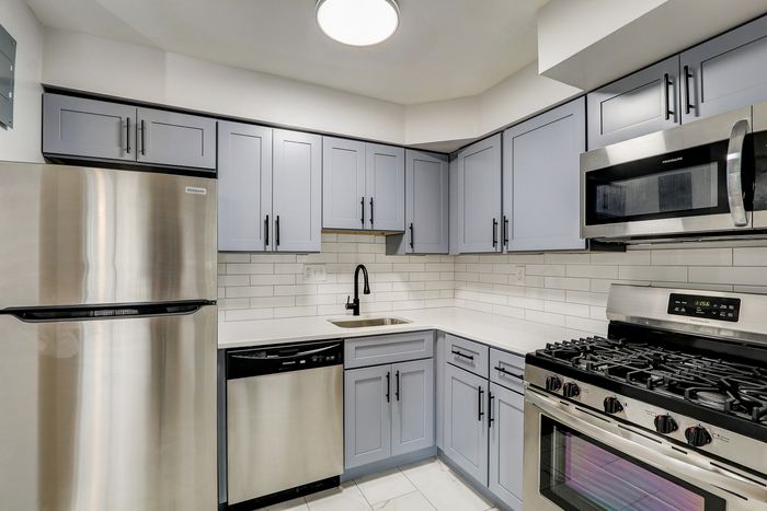 Modern kitchen with sleek stainless steel appliances, elegant light grey cabinets, and a contemporary subway tile backsplash.