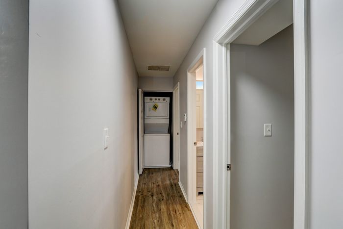 Charming hallway featuring modern wood flooring, leading to a convenient in-unit laundry area with washer and dryer.