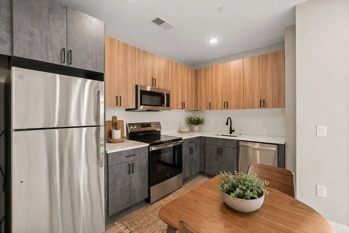 Modern kitchen with sleek stainless steel appliances, stylish two-tone cabinets, and elegant wooden dining table with a decorative planter.