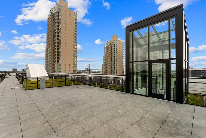 Modern rooftop terrace with stunning cityscape views and glass structure under a bright blue sky.