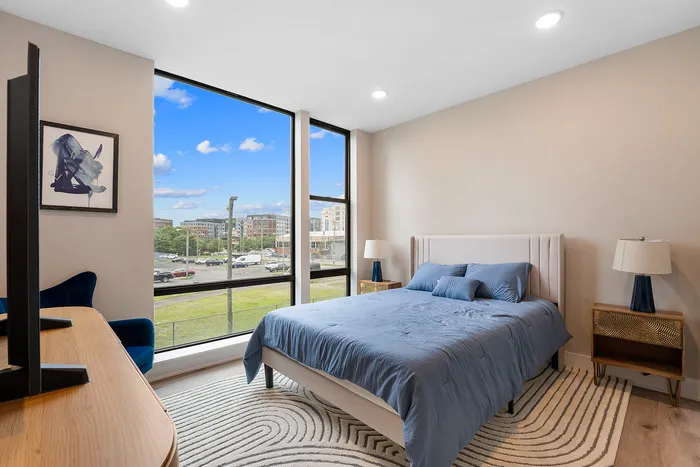 Chic bedroom with floor-to-ceiling windows, elegant blue bedding, and contemporary decor offering vibrant city views.
