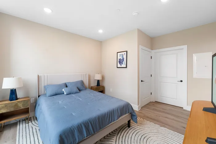 Bright and inviting bedroom featuring a plush bed with blue bedding, stylish wood nightstands, and modern decor.