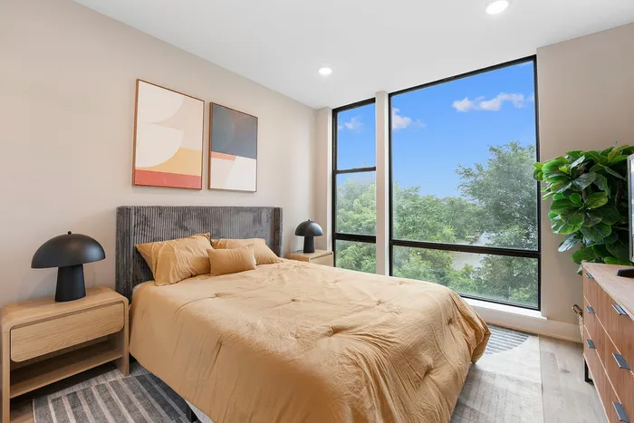 Bright and inviting bedroom with modern decor, featuring a large window providing scenic views of lush greenery.