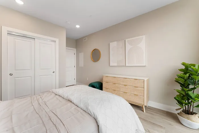 Modern bedroom with minimalist design featuring a cozy bed, artistic wall decor, sleek dresser, and vibrant green plant.