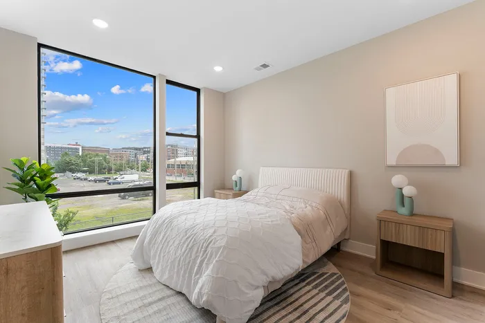 Bright and airy bedroom with large windows, modern decor, and a serene view of the cityscape, perfect for urban living.