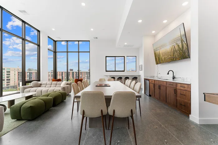 Chic apartment communal space with panoramic city views, featuring modern furniture, expansive windows, and a stylish kitchenette.
