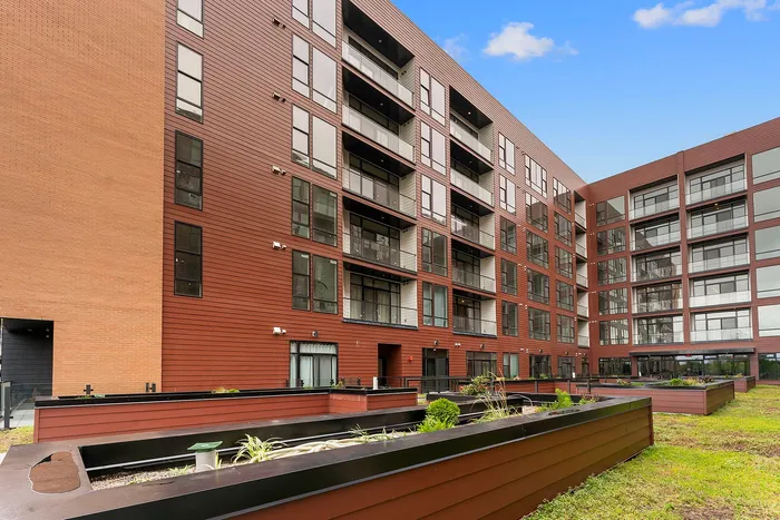 Modern apartment building with sleek red brick exterior and expansive balconies, surrounded by lush greenery.