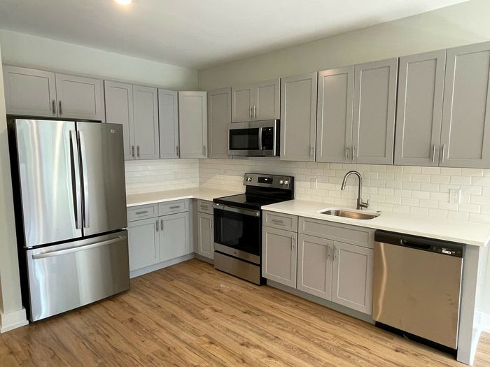 Modern kitchen with sleek stainless steel appliances, elegant gray cabinetry, and stylish wood flooring.