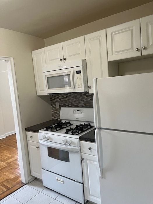 Modern kitchen with white cabinets, a full-size refrigerator, gas stove, and built-in microwave in a cozy apartment setting.