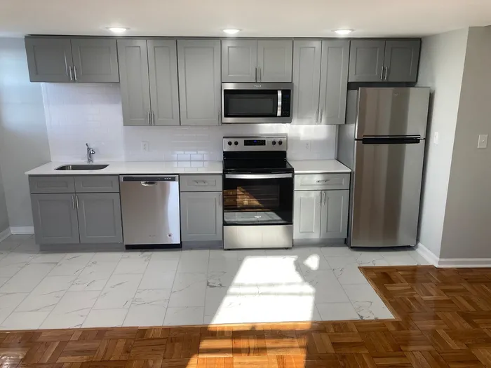 Modern kitchen with sleek gray cabinets, stainless steel appliances, and elegant tile and wood flooring.
