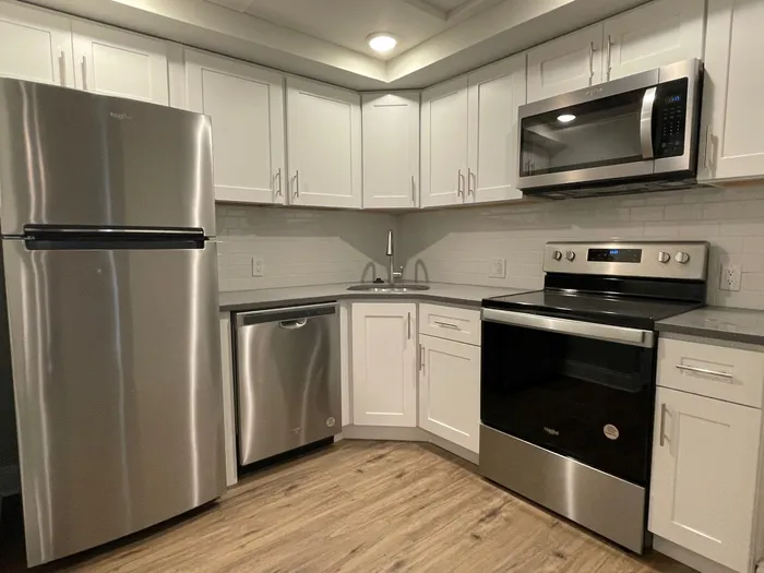 Modern kitchen with sleek stainless steel appliances, white cabinetry, and elegant wood flooring.