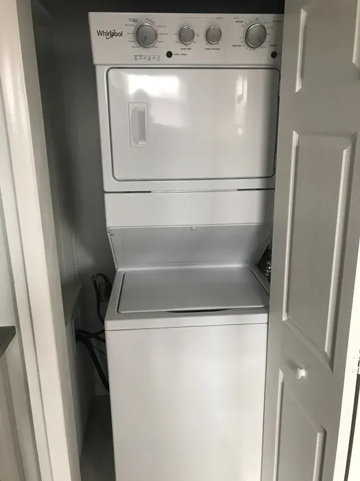 Modern built-in apartment laundry area featuring a sleek white Whirlpool stacked washer and dryer behind a partially open door.