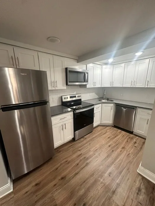 Modern kitchen with sleek stainless steel appliances, elegant white cabinetry, and beautifully polished wood flooring.