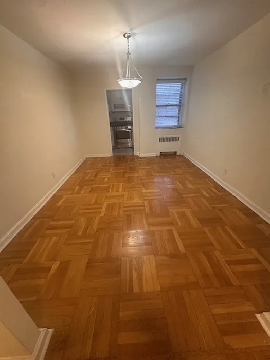 Bright dining area with elegant parquet flooring, featuring a modern light fixture and a doorway leading to a cozy kitchen. Perfect for stylish living and entertaining.