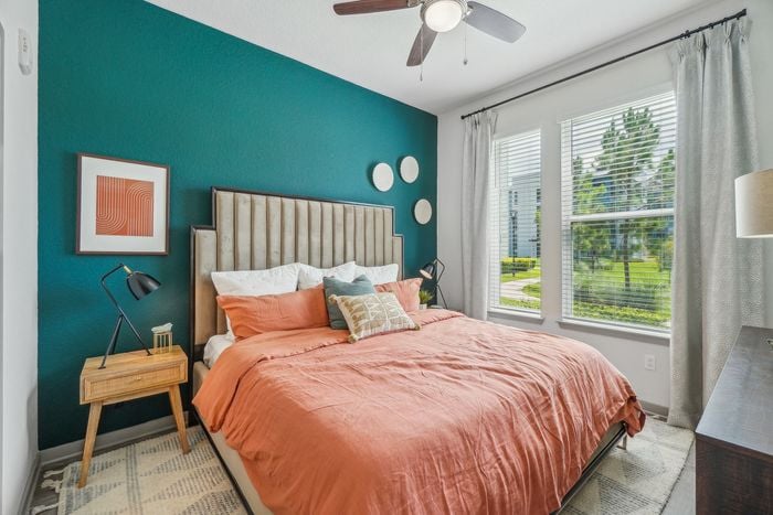 Inviting bedroom with lush garden views, featuring a stylish emerald accent wall, contemporary artwork, and warm coral bedding.