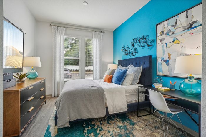 Bright and inviting bedroom with a modern blue accent wall, featuring a stylish bed with colorful pillows, elegant artwork, and a sleek work desk.