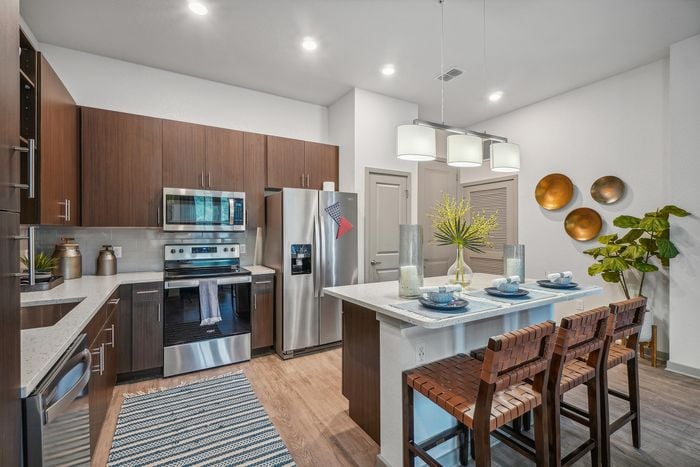 Modern kitchen with sleek dark wood cabinetry, stainless steel appliances, and a stylish island with seating, accented by elegant pendant lighting and contemporary decor.