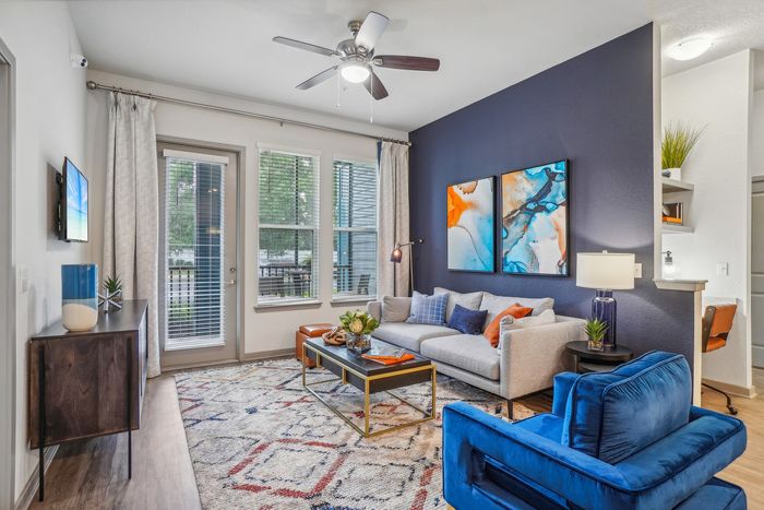 Contemporary living room with a vibrant navy accent wall, modern artwork, and plush seating, boasting ample natural light from large windows.