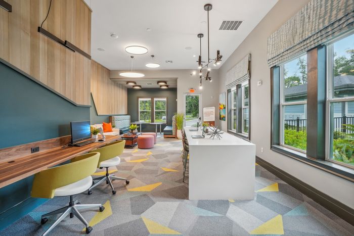 Bright and modern communal workspace with vibrant geometric carpet, stylish lighting, and lush outdoor views.