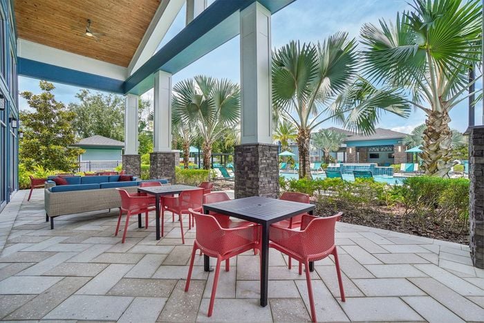 Elegant outdoor seating area with vibrant red chairs overlooking a pristine pool surrounded by lush palm trees and modern architecture.