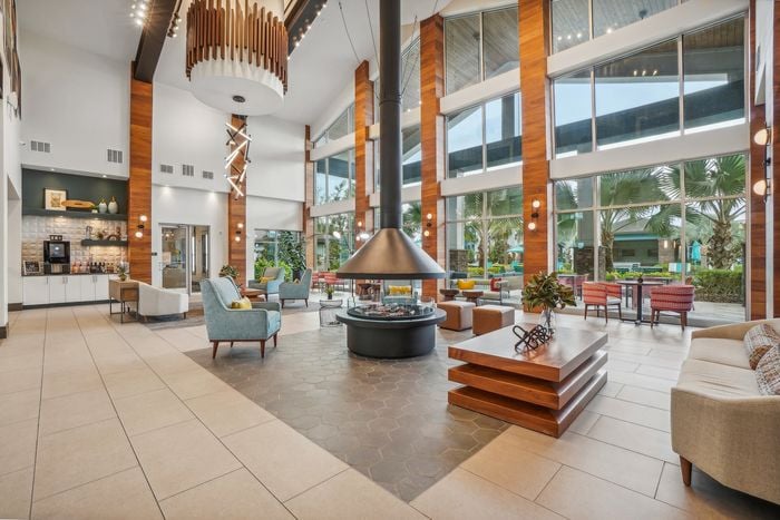 Stunning luxury apartment lobby featuring high ceilings, floor-to-ceiling windows, modern fireplace, and stylish furnishings with vibrant accents.