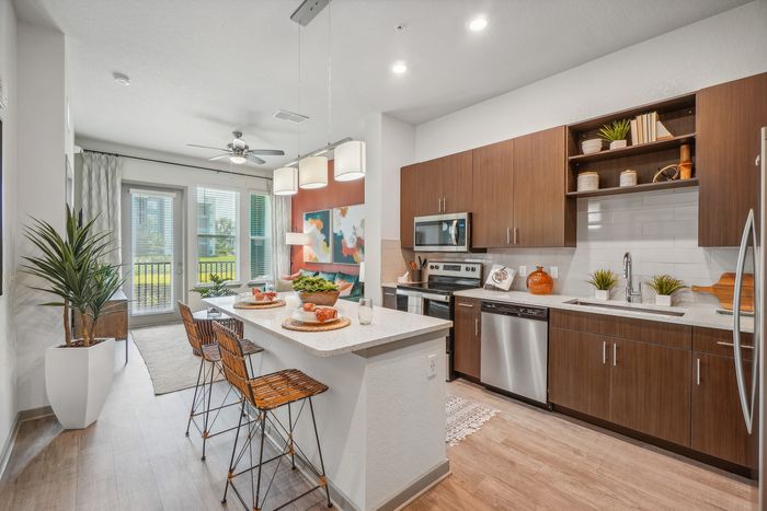 Modern kitchen with sleek wooden cabinetry, stainless steel appliances, and an inviting breakfast bar with stylish seating. Bright and airy living area with patio access and tasteful artwork accents.