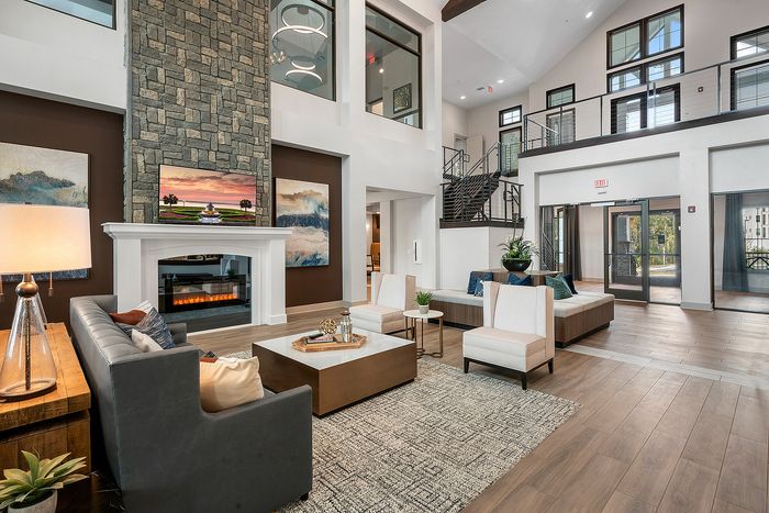 Luxurious open-concept living area with a stunning stone fireplace, modern furnishings, and elegant decor in a spacious, high-ceilinged apartment.