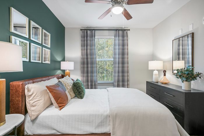 Inviting bedroom with plush bedding, cozy pillows, and elegant decor, highlighted by a deep green accent wall and sophisticated lighting.