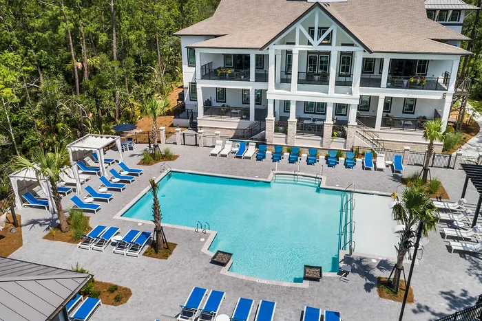 Luxurious apartment complex with a stunning large swimming pool, surrounded by sleek lounge chairs and lush greenery, offering a perfect blend of relaxation and elegance.