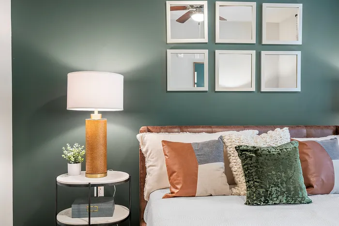 Stylish bedroom featuring a sophisticated green accent wall, elegant pillows, and a chic side table with a decorative lamp.