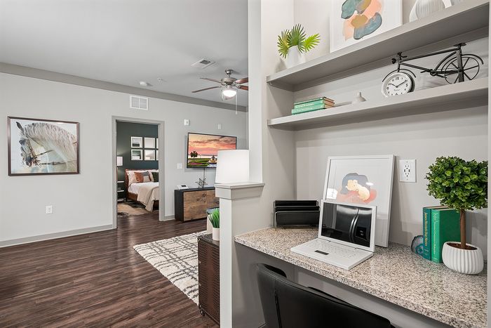 Chic apartment interior showcasing modern home office space with built-in desk, stylish shelving, and a peek into a cozy bedroom with elegant decor.