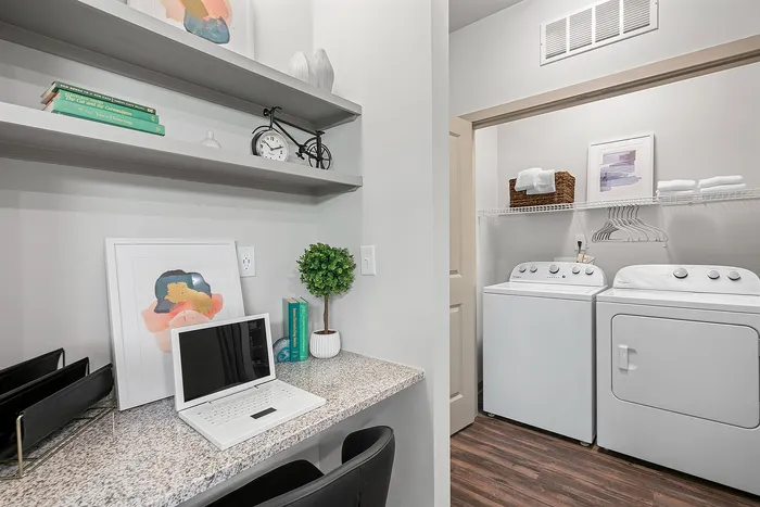 Chic home office nook adjacent to a modern laundry room with washer and dryer, showcasing sleek design and practicality.