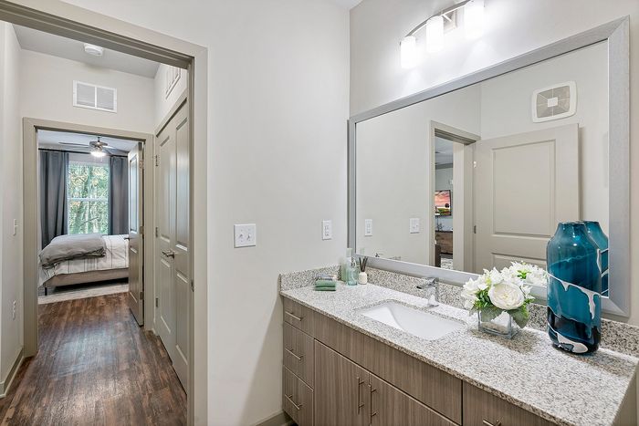 Bright and modern bathroom featuring a sleek granite countertop, elegant fixtures, and a decorative blue vase next to fresh flowers with a glimpse into a cozy bedroom with natural light.