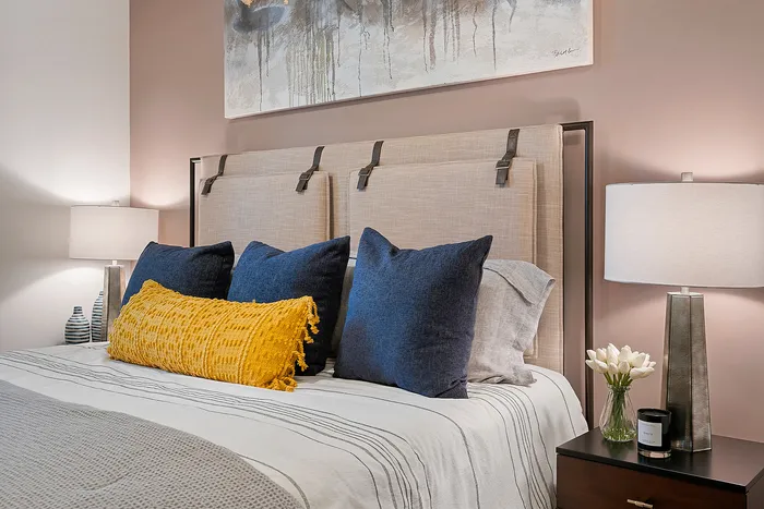 Inviting bedroom design with elegant, textured headboard, cozy blue and yellow pillows, ambient lighting, and a modern nightstand with decorative accents.