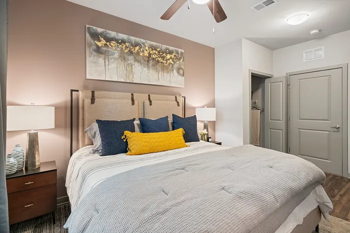 Elegant bedroom featuring a plush bed with navy and yellow cushions, stylish lamps, and modern art, exuding comfort and luxury.