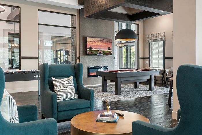 Modern recreational area with plush teal armchairs, a sleek pool table, and vibrant wall art, perfect for relaxation and entertainment.