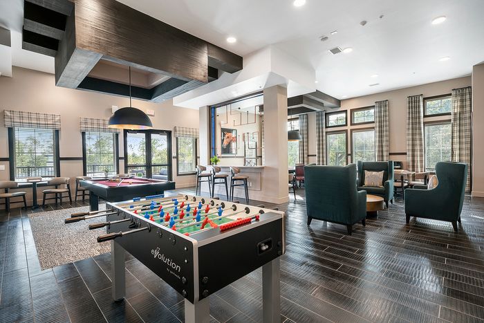 Modern communal lounge featuring sleek foosball and pool tables, comfortable seating, and elegant window views.