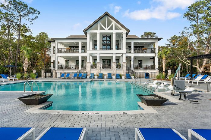 Luxurious apartment complex featuring a sparkling swimming pool, surrounded by elegant lounge chairs and a modern, stylish building with spacious balconies.