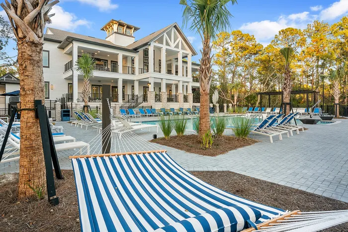 Luxurious apartment complex with a refreshing pool, surrounded by blue lounge chairs and palm trees, perfect for relaxation and leisure.