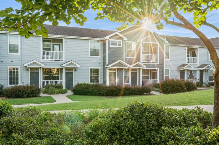 Charming townhouses with inviting porches, nestled in lush greenery and warmed by a golden sunburst.