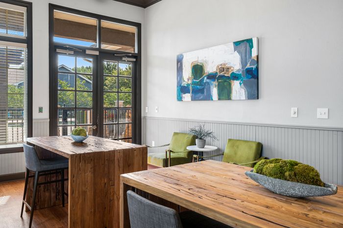 Bright and inviting modern dining area with rustic wooden tables, green accent chairs, and large windows overlooking lush greenery.