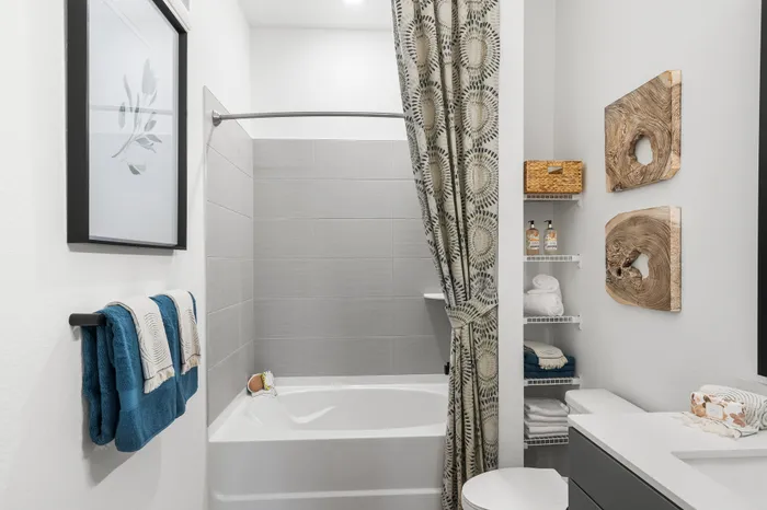 Elegant bathroom with modern tub, artistic wall decor, stylish tile design, and neatly organized shelves for a cozy atmosphere.