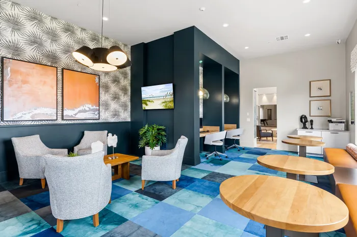 Modern communal lounge with chic gray seating, vibrant artwork, and contemporary workspace area, ideal for leisure and productivity.